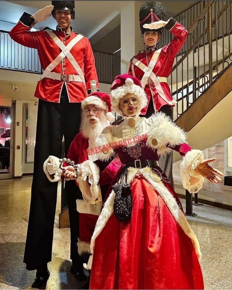 Corporate Santa in Oklahoma City: Santa and Mrs. Claus with two nutcracker soldiers on stilts indoors.