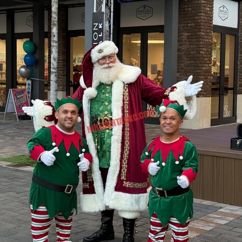 Santa Claus impersonator for hire in Oklahoma City in a burgundy coat with two elves giving a thumbs-up.