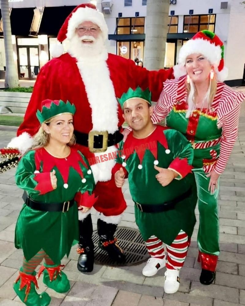 Santa for hire in Moore, OK standing with three elves at dusk in front of string lights.